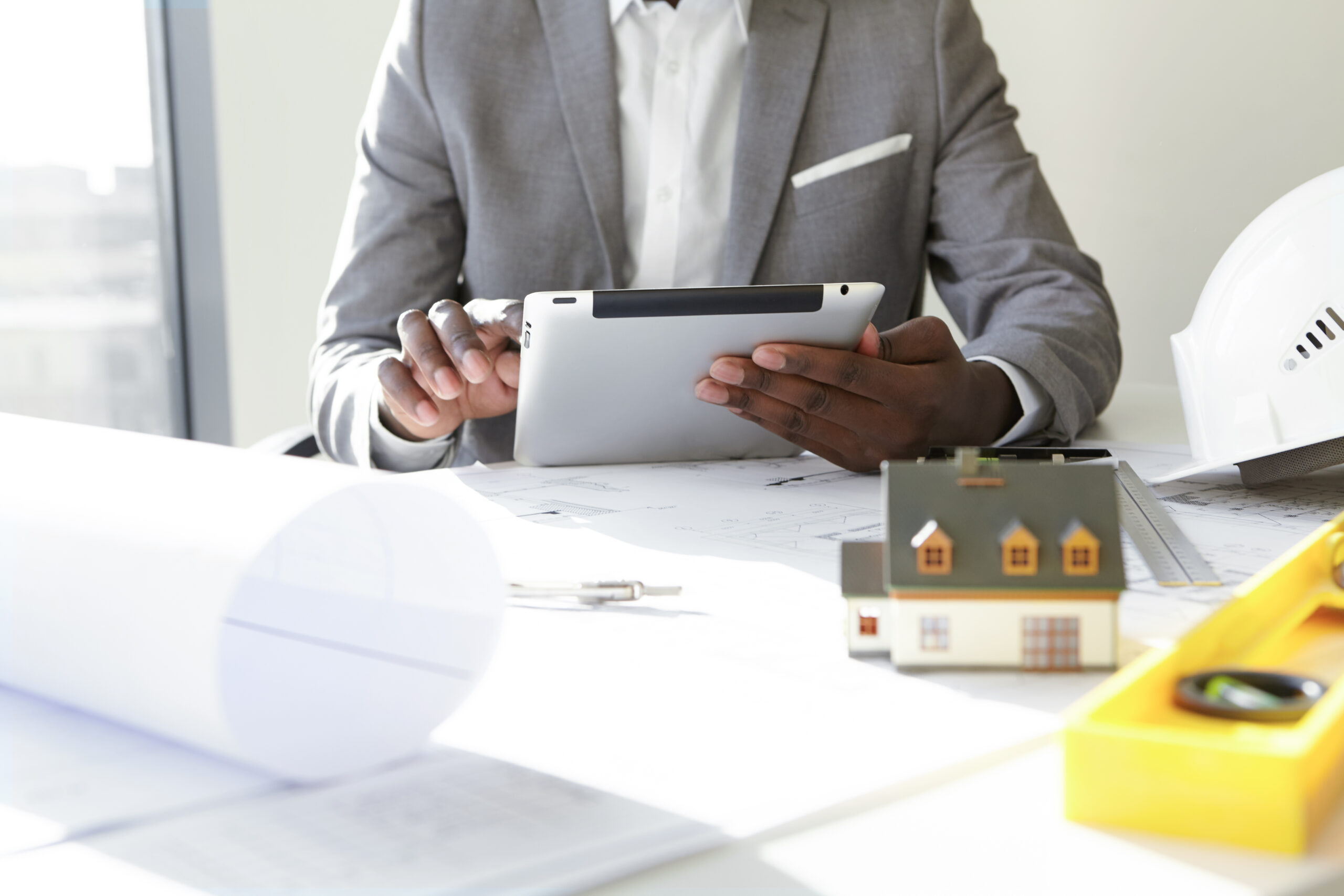 Property investor reviewing figures on a tablet beside building plans and a house model
